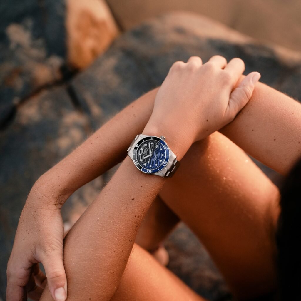 Mujer con reloj Mido Ocean Star 39 sobre rocas en la playa, verano.